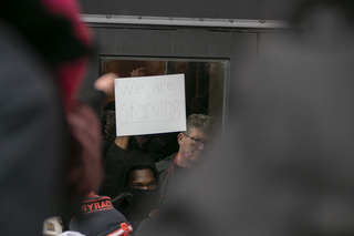 Feb. 18: Department of Public Safety officer Joe Shanley guards the entrance of Crouse-Hinds Hall while a #NotAgainSU organizer inside holds up a sign that reads “We are starving.” In an attempt to get #NotAgainSU protesters to leave Crouse-Hinds, DPS sealed the building and prevented people from bringing food or resources to the organizers. The movement occupied the building to continue its protest of SU’s response to hate incidents on and near campus.